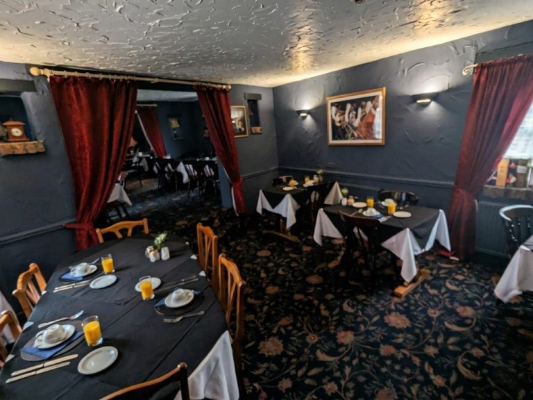 Cosy dining area with tables set for a meal, featuring dark decor and warm lighting.